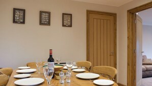 A dining room with a round wooden table set for six, framed pictures on the wall, and a wooden door. - 2 bedroom accommodation in Nosterfield, near Masham (Nosterfield, near Masham)