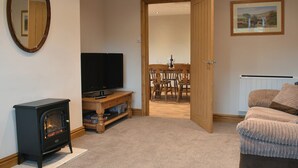 A living room with a fireplace, a television, a dining area with chairs, and a couch. - 2 bedroom accommodation in Nosterfield, near Masham (Nosterfield, near Masham)