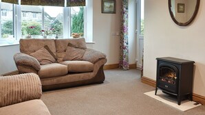 A cozy living room with a sofa, a fireplace, and a large window with curtains. - 2 bedroom accommodation in Nosterfield, near Masham (Nosterfield, near Masham)