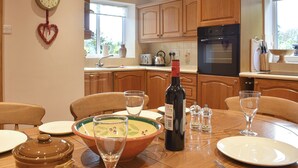 A kitchen with wooden cabinets, a stove, and a dining table set with plates, glasses, and a bottle of wine. - 2 bedroom accommodation in Nosterfield, near Masham (Nosterfield, near Masham)