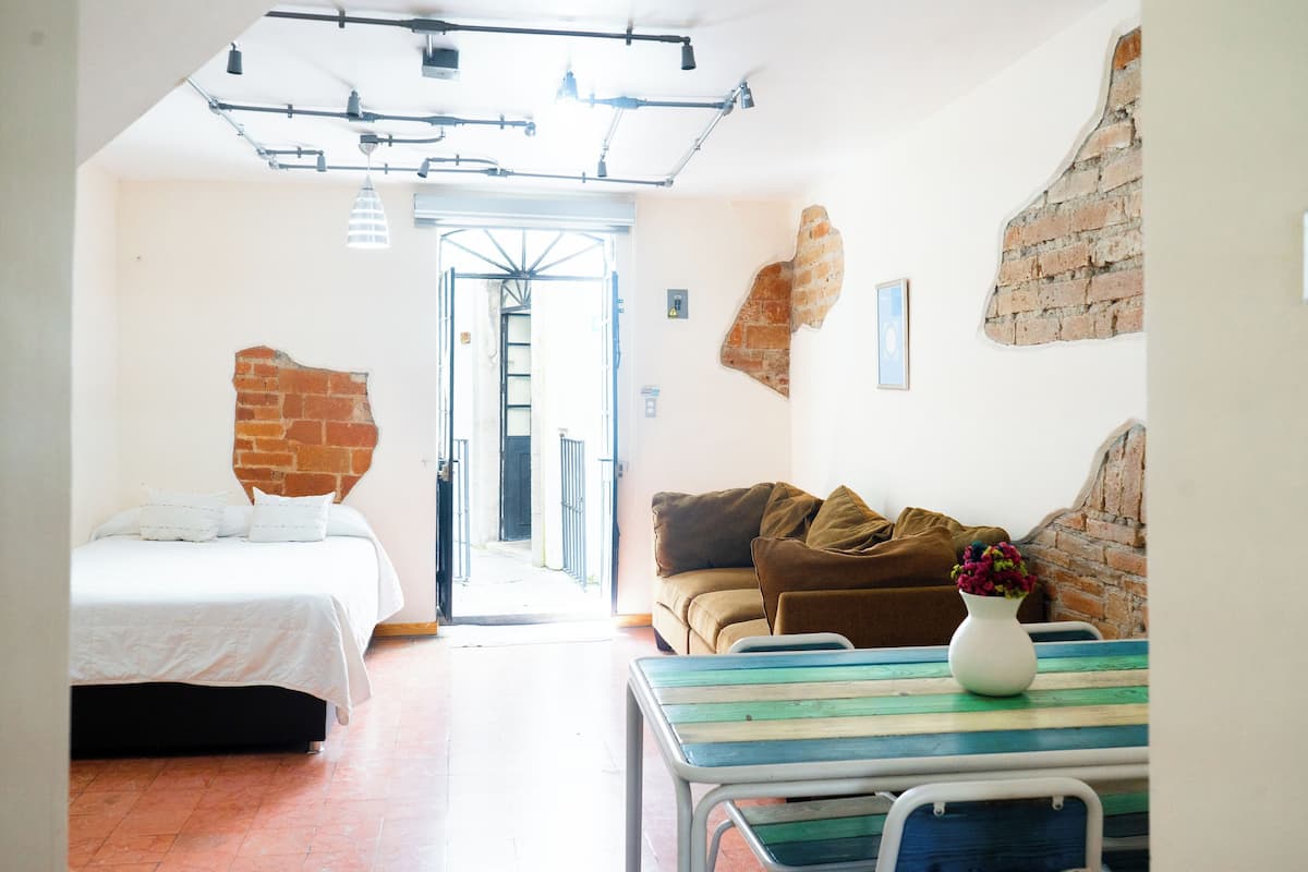 Una habitación con una cama, un sofá, una mesa con un florero y una pared de ladrillo.