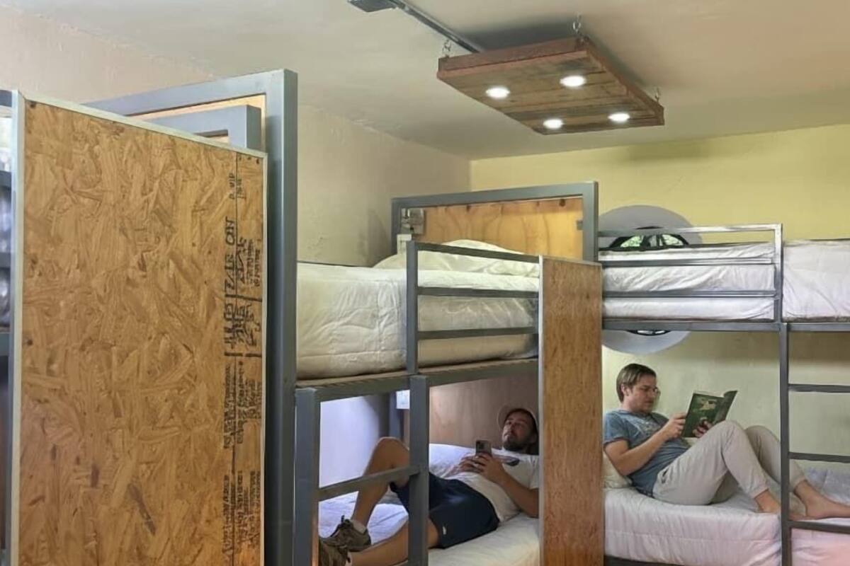 Dormitorio con literas, cabeceros de madera, barandillas de metal e iluminación empotrada en el techo.
