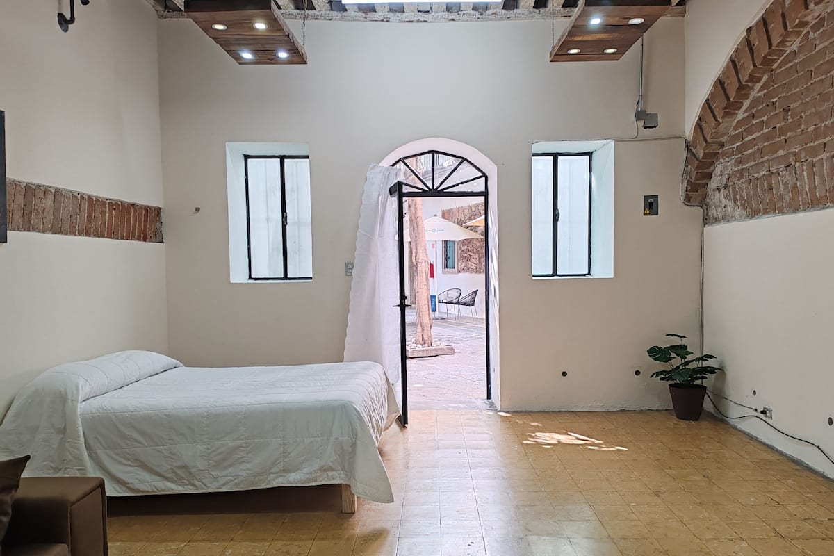 Un dormitorio con cama, una planta en maceta y vistas a un espacio exterior por una puerta abierta.