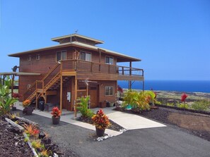A two-story wooden house with a balcony, a staircase, and a view of the ocean. - Milolii Whale House with Spectacular Ocean View! (Captain Cook)