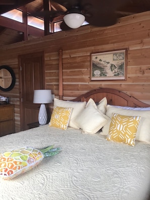 Une chambre à coucher dans une cabane en bois, avec un lit, des oreillers, une carte accrochée au mur et un ventilateur de plafond.