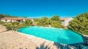 A swimming pool with a stone deck, surrounded by stone buildings and lush greenery.
