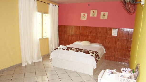 A bedroom with a bed, a fan, and a window with curtains. - Hotel Bonança (Samambaia)