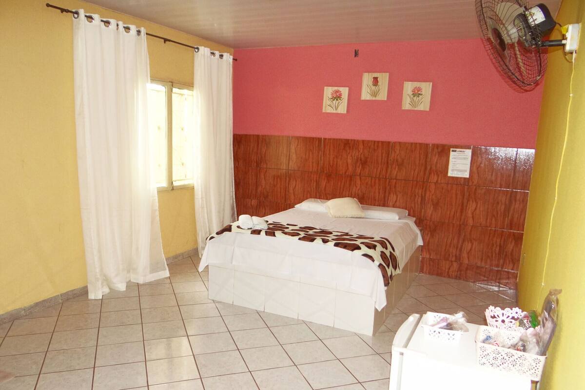 A bedroom with a bed, a fan, and a window with curtains.