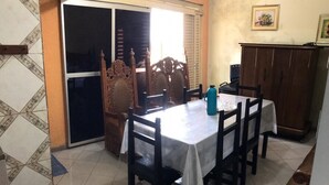 A dining area with a table set for four, surrounded by chairs, a cabinet, and a sliding glass door leading to a balcony. - Hotel Bonança (Samambaia)