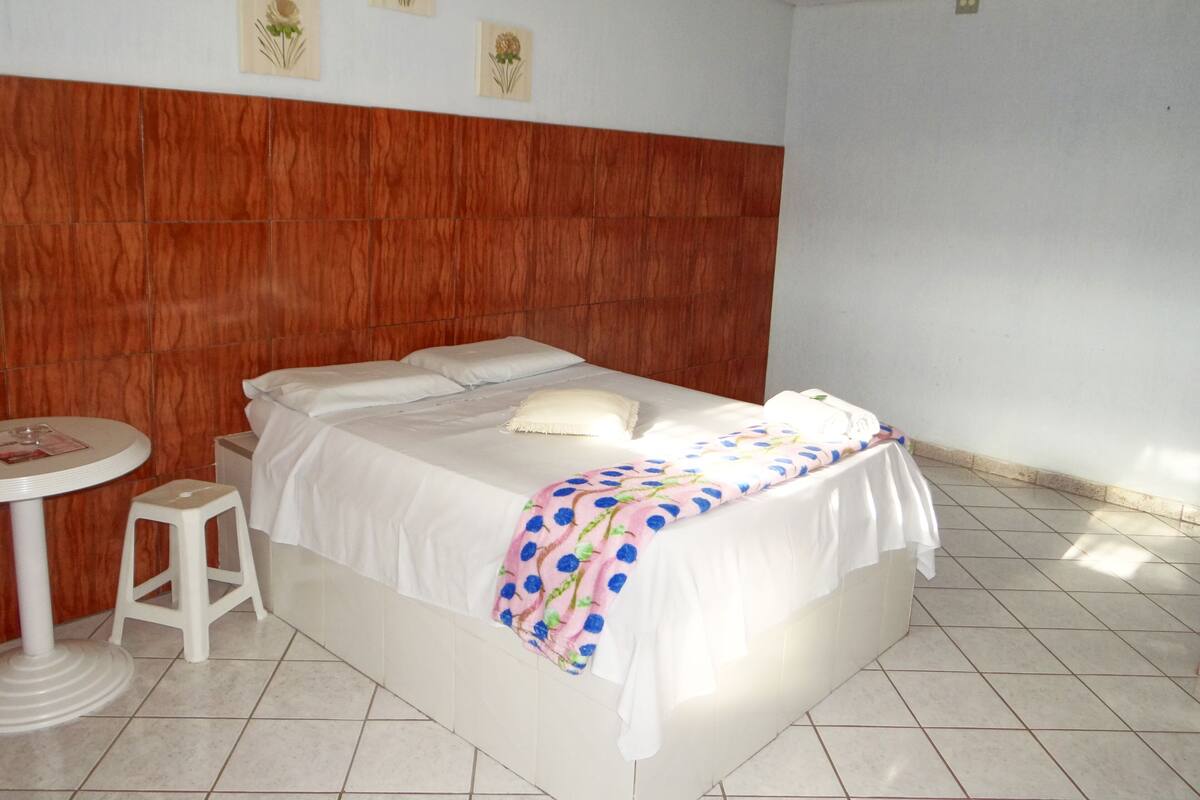 A hotel room with a wooden headboard, a bed with white linens, a small round table, and a single stool.