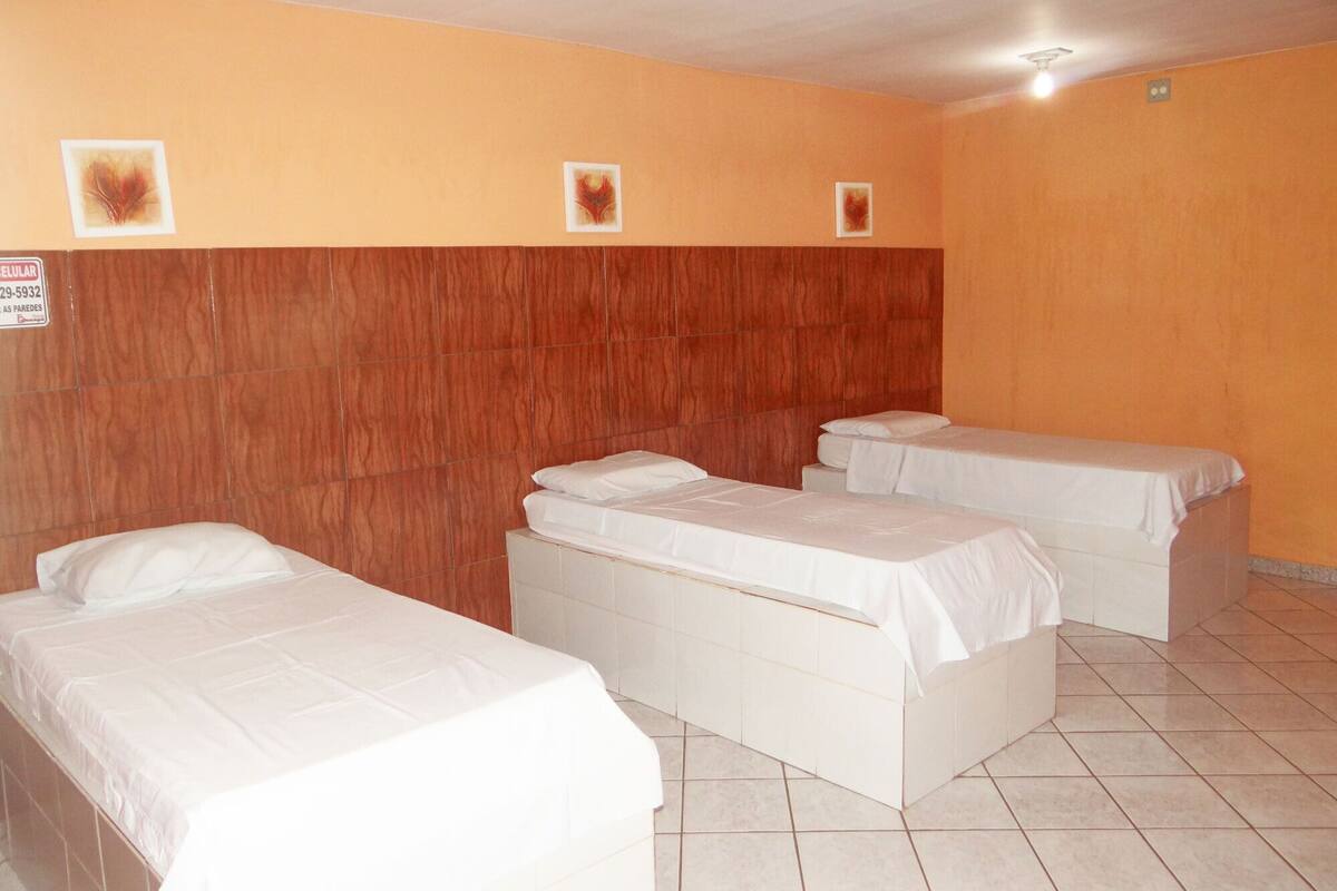 A hotel room with three single beds, a wooden headboard, and a tiled floor.