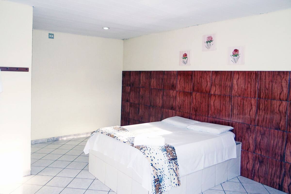 A hotel room with a bed, a wooden headboard, and a tiled floor.