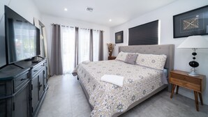 A modern bedroom with a large bed, a TV, a dresser, and a bedside table with a lamp. - Luxury Water Front Villa! (Pompano Beach)