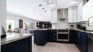 A modern kitchen with dark blue cabinets, stainless steel appliances, and a marble countertop. - Luxury Water Front Villa! (Pompano Beach)