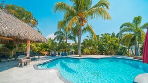 A swimming pool with a thatched roof structure, surrounded by palm trees and outdoor furniture. - Luxury Water Front Villa! (Pompano Beach)