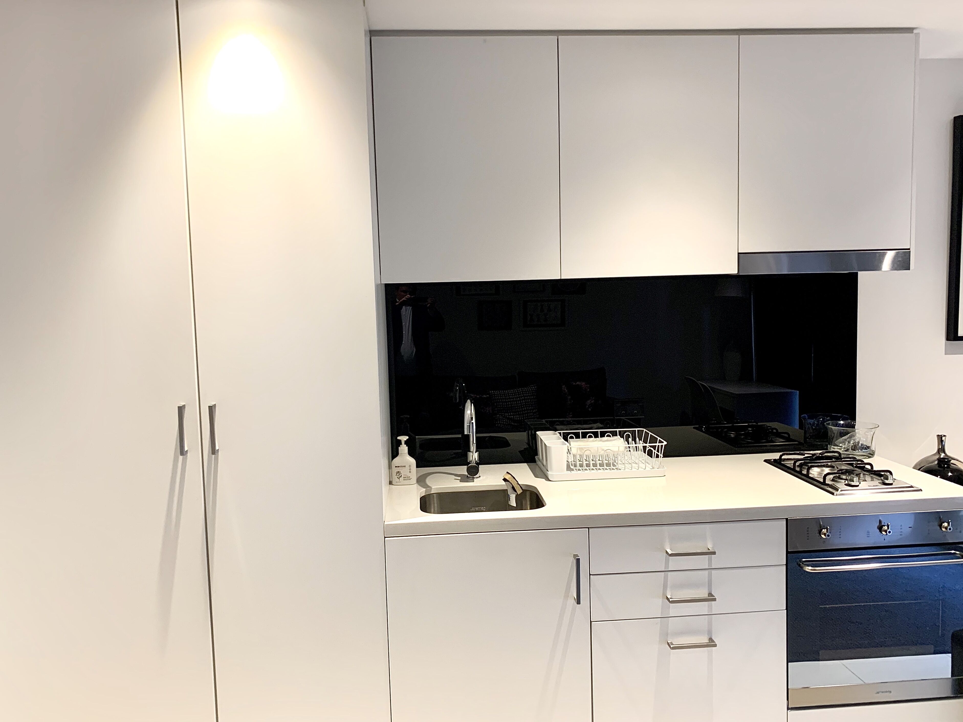 Una cocina moderna con armarios blancos, una campana extractora de acero inoxidable, horno empotrado y un lavabo con escurreplatos.
