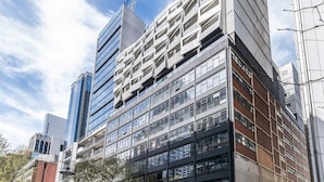 Un edificio moderno con varios pisos, amplias ventanas y un letrero de estacionamiento que indica una zona de estacionamiento público.