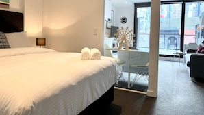 Habitación de hotel con cama, escritorio, silla y vista a la ciudad a través de un ventanal.