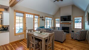 A spacious living area with a dining table, sofa, and patterned armchair. A fireplace and television are visible. - Beautiful New Home!! (Intervale)