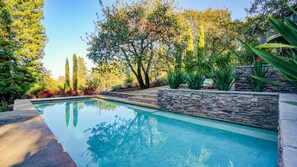 A swimming pool with stone steps leading into it, surrounded by lush greenery and trees. - Sebastopol Luxury Home With Views, Pool & Hot tub (Sebastopol)