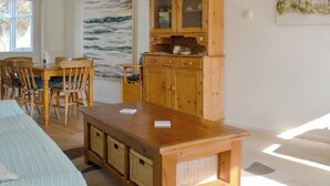 A dining area with wooden chairs and a table, a wooden cabinet with glass doors, and a large abstract painting on the wall. - 3 bedroom accommodation in Sheringham (Sheringham)