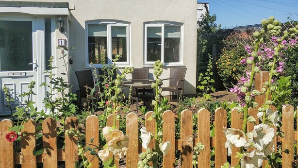 A house with a white exterior, a wooden fence, and a garden with various plants and flowers. - 3 bedroom accommodation in Sheringham (Sheringham)