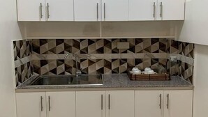 Une cuisine compacte avec des meubles blancs, un pare-feu géométrique et un évier en acier inoxydable.