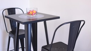 Une petite table sur laquelle est posé un vase en verre contenant des fleurs, deux chaises noires et, en arrière-plan, un mur blanc.