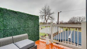 A balcony with a green artificial hedge, a white railing, and a grey sofa.