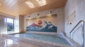 A hot spring area with a mural of Mount Fuji and waves, tiled walls, and a wooden ceiling.