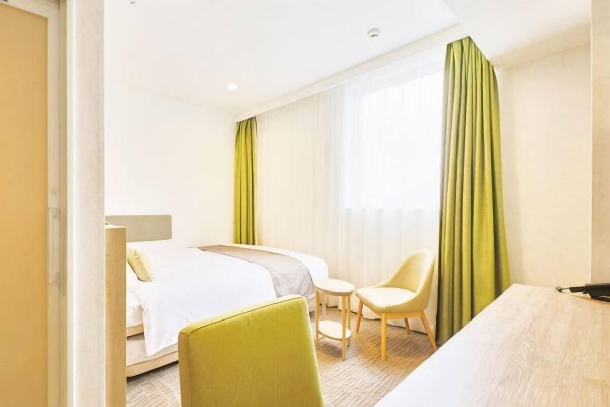 A hotel room with a bed, a desk, a chair, and a window with curtains.