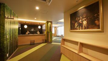 A hotel lobby with a reception desk, a large painting on the wall, and a colorful carpet.