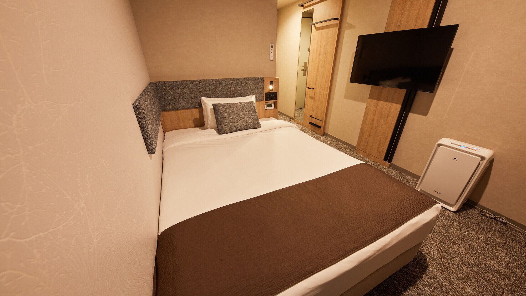 A hotel room with a bed, a TV, a mini-fridge, and a wooden wardrobe.