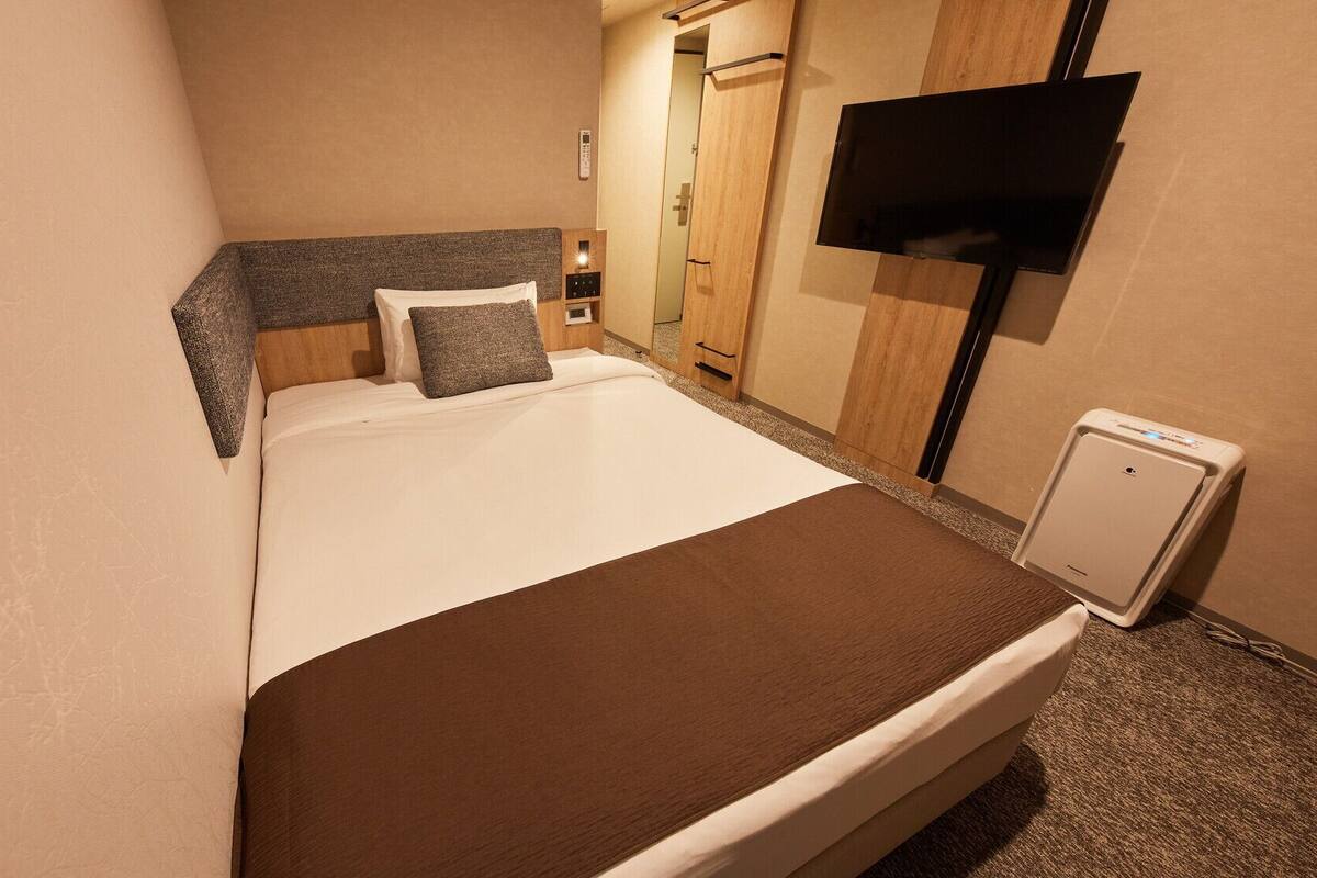A hotel room with a bed, a TV, a mini-fridge, and a wooden wardrobe.