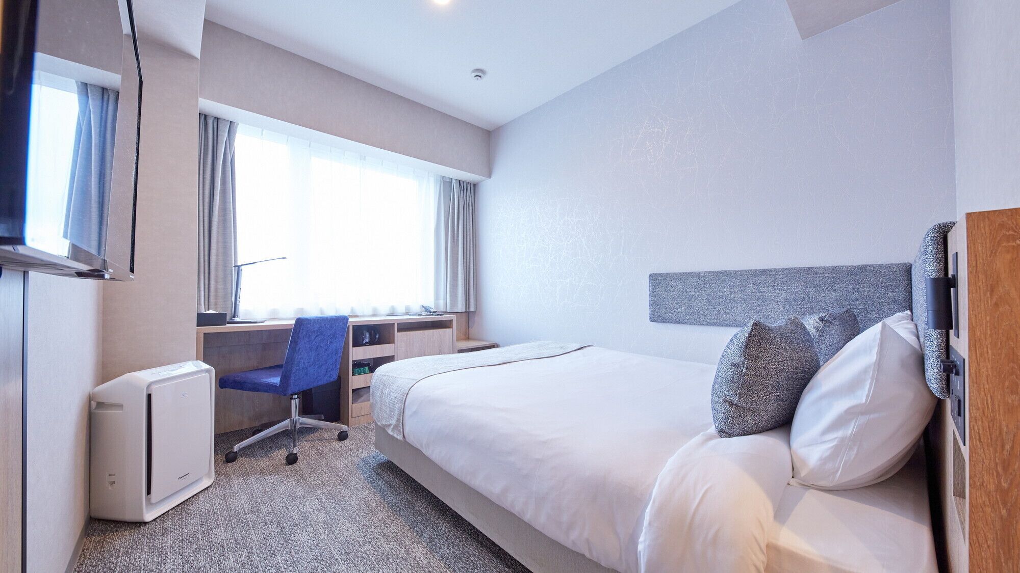 A hotel room with a bed, a desk, a chair, and a window.