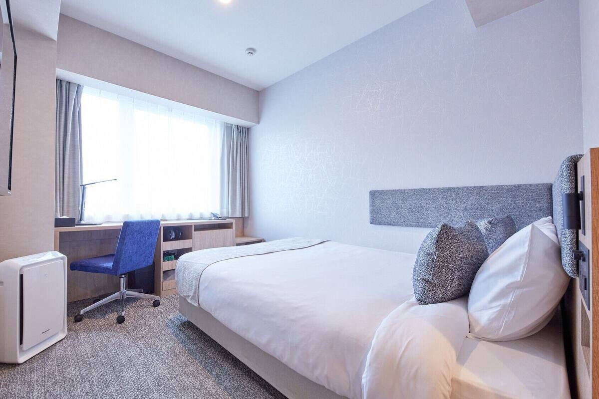 A hotel room with a bed, a desk, a chair, and a window.