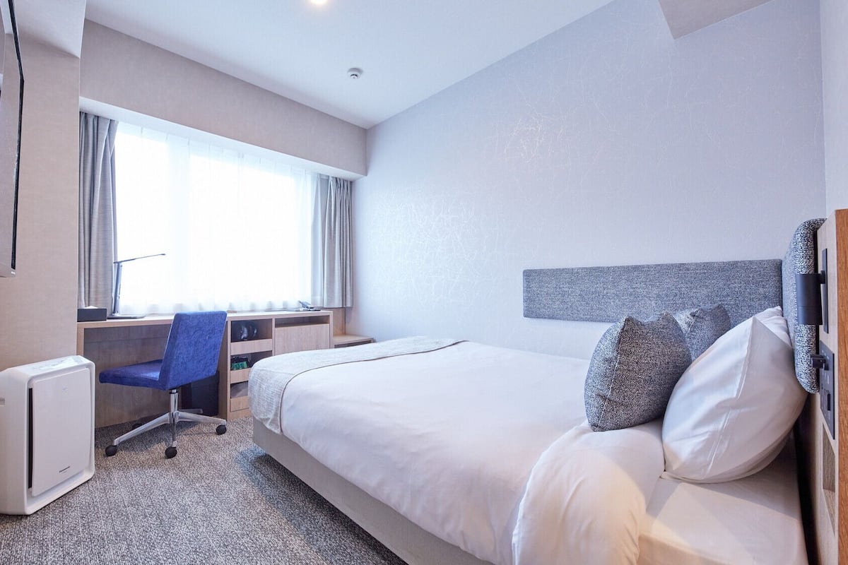 A hotel room with a bed, a desk, a chair, and a window.