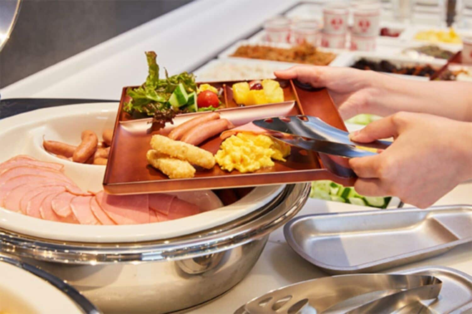 Un buffet proposant une variété de plats, notamment du jambon, des saucisses, des œufs brouillés et une salade.