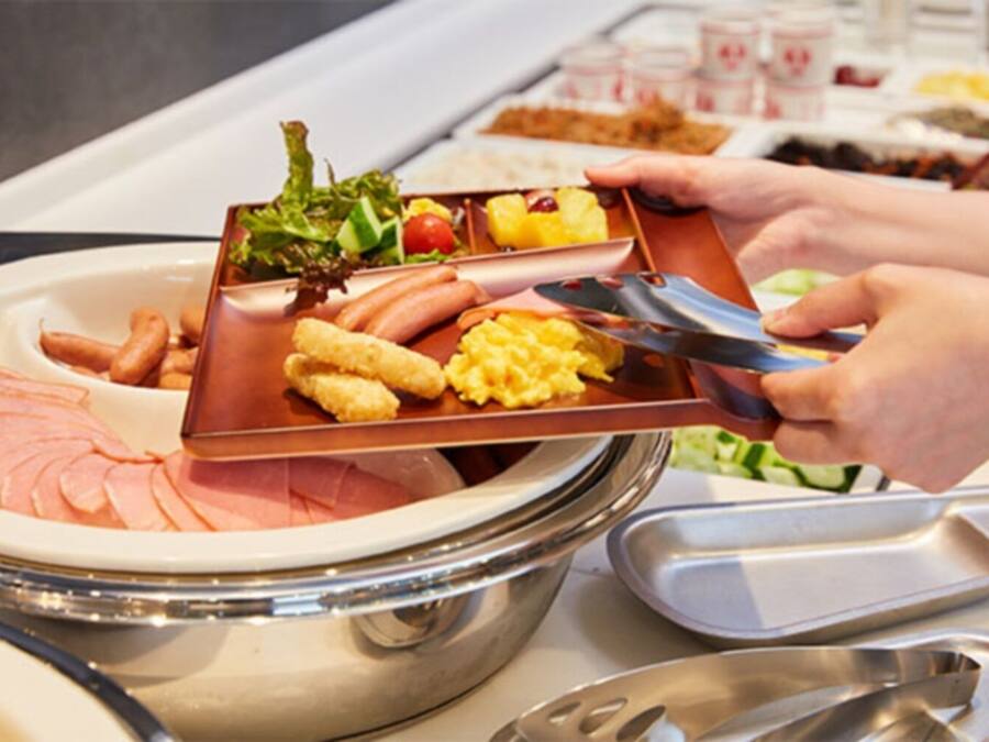 A buffet setup with various food items including ham, sausages, scrambled eggs, and a salad.
