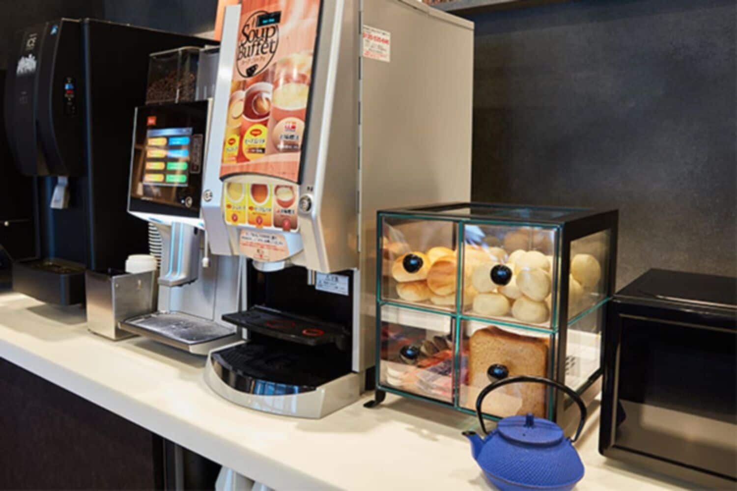 Máquina de café, placa indicando buffet de sopas e uma vitrine de vidro com alimentos.
