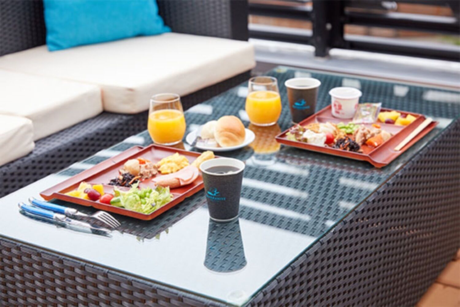 A dining table with two trays of food, a glass of orange juice, and a coffee cup.