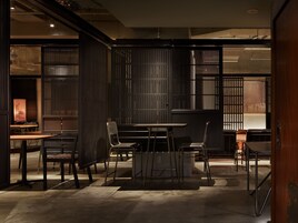 Un interior moderno con comedor, que incluye una mesa y sillas, zona de cocina con estufa, y vista al exterior a través de una ventana.