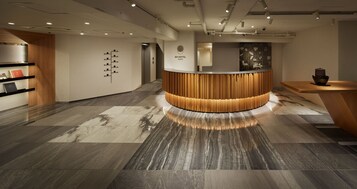 Zona de recepción de un hotel con un mostrador de madera, un panel informativo en la pared y suelo de baldosas.