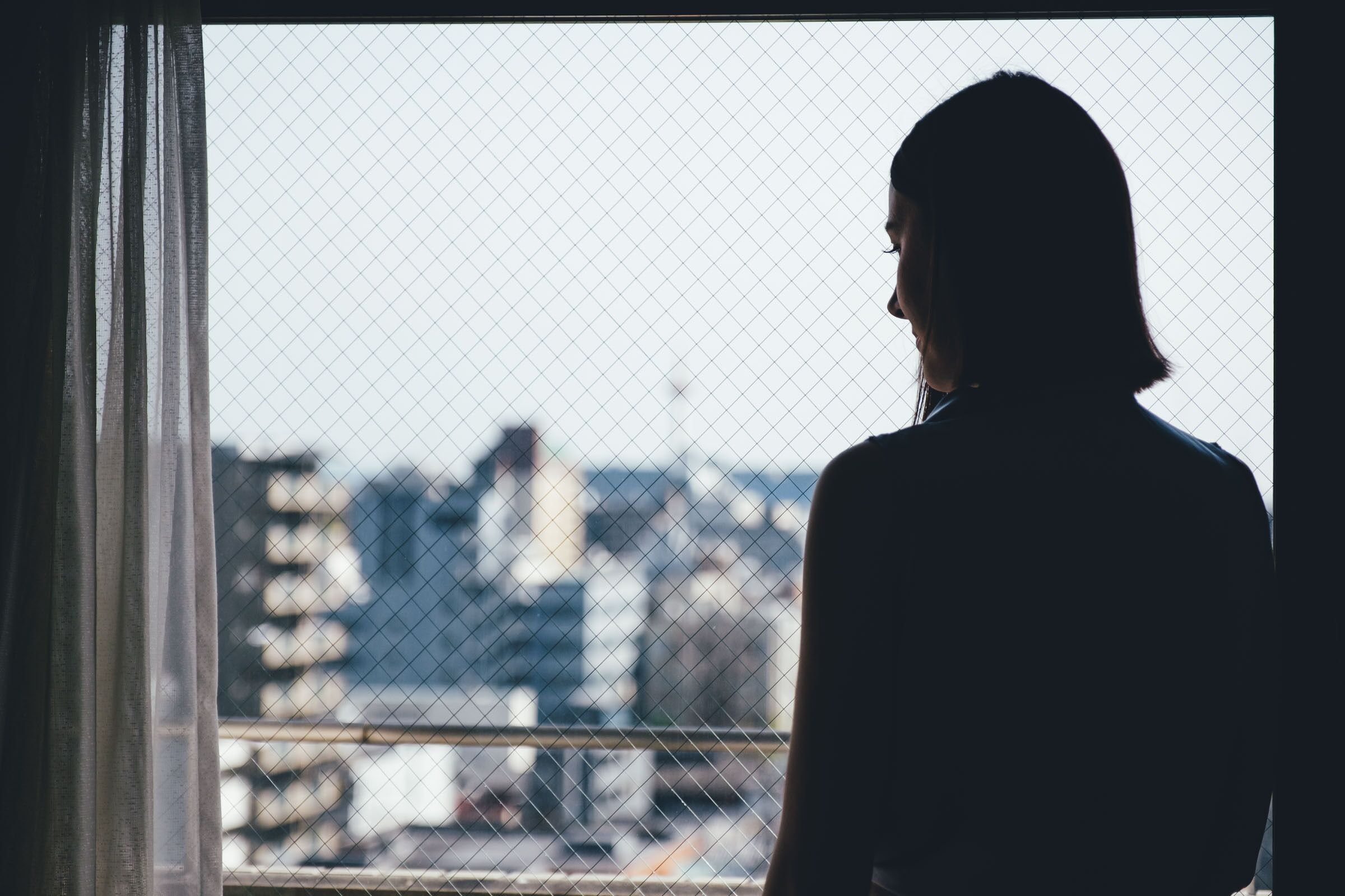 Una persona de pie junto a una ventana con vistas a un paisaje urbano.