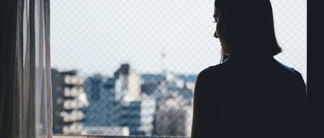 Una persona de pie junto a una ventana con vistas a un paisaje urbano.