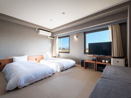 Habitación de hotel con dos camas, televisión y un ventanal con vistas.