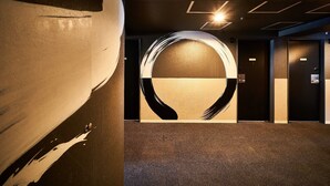 Un vestíbulo moderno de hotel con un gran cuadro abstracto en la pared, una lámpara circular y suelo alfombrado.