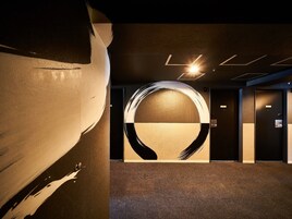 Un vestíbulo moderno de hotel con un gran cuadro abstracto en la pared, una lámpara circular y suelo alfombrado.