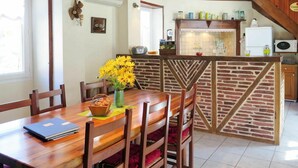 A dining area with a wooden table and chairs, a vase of yellow flowers, and a kitchen area with a brick wall and various kitchen appliances. - Stunning private villa for 5 guests with private pool, A/C, TV, terrace and panoramic view (La Grèze)