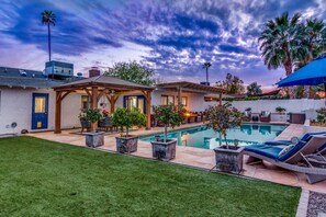 A backyard with a swimming pool, outdoor furniture, and a covered patio area.